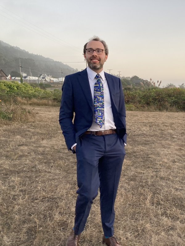 Paul in a blue suit standing in a golden field at dusk